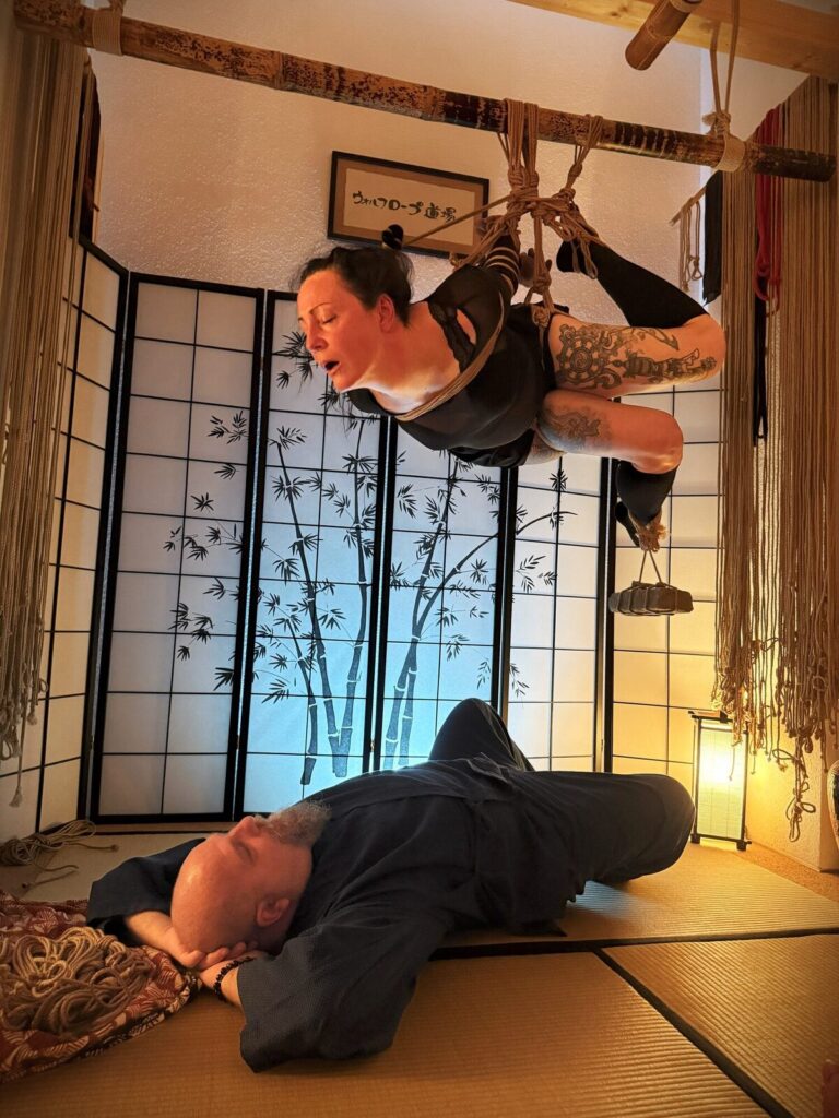 Hängefesselung im Kinbaku Salon, darunter liegt der Rigger auf der Tatami
