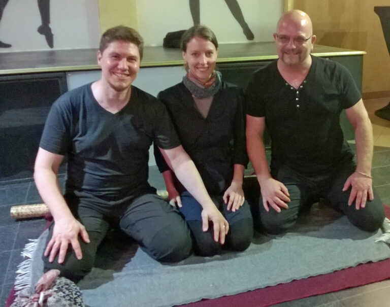 Erinnerungsfoto: drei Personen knien lächelnd nebeneinander auf einer Decke nach dem Workshop
