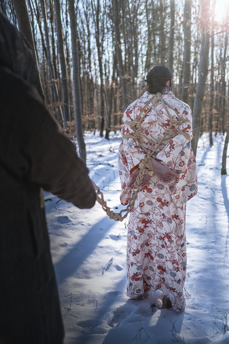 Im geblümten Kimono im verschneiten Wald, gebundene Hände, der Rigger hält das Seil