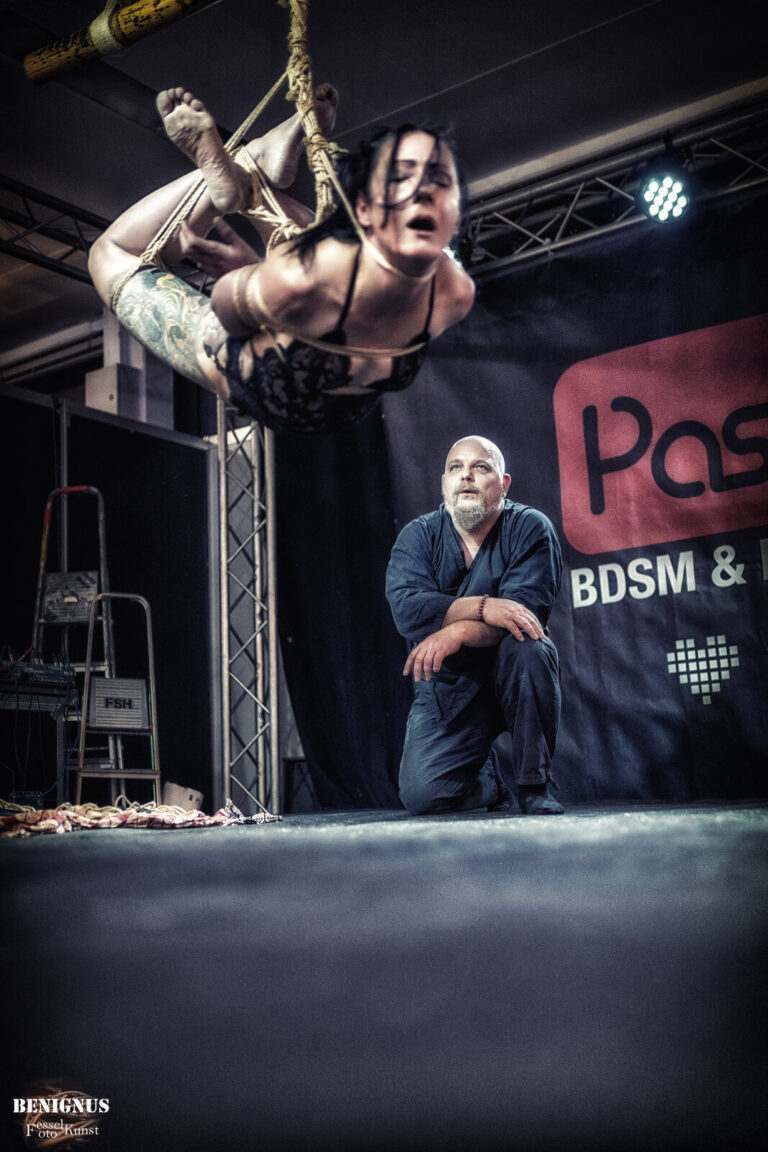 Hängefesselung hoch unter dem Bambus, der Rigger kniet auf der Bühne und schaut zu, Passion 2021