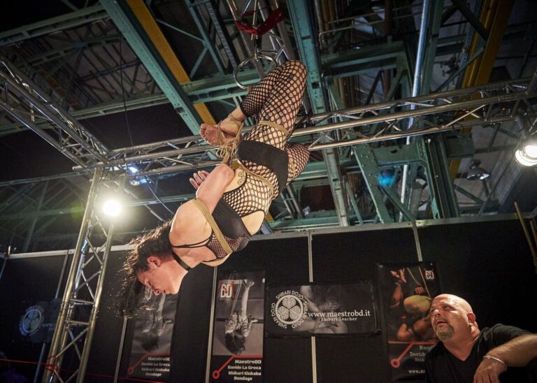 Hängefesselung im Netz-Outfit unter dem Stahldach der Halle, der Rigger schaut von unten zu, BoundCon 2018