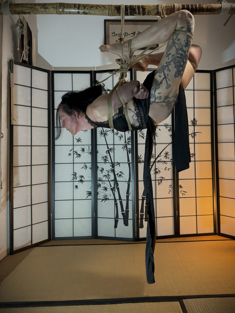 Hängefesselung, ein tätowiertes Bein nach oben gezogen, ein schwarzes Tuch hängt herab