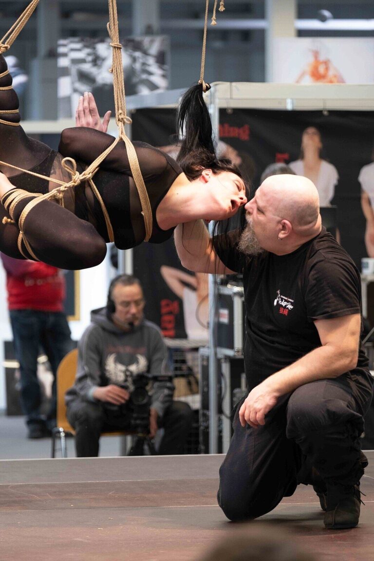 Kuss: Das Model schwebt waagerecht im Seil, der Rigger kniet davor, Bondage-Fetish-World Spring 2023