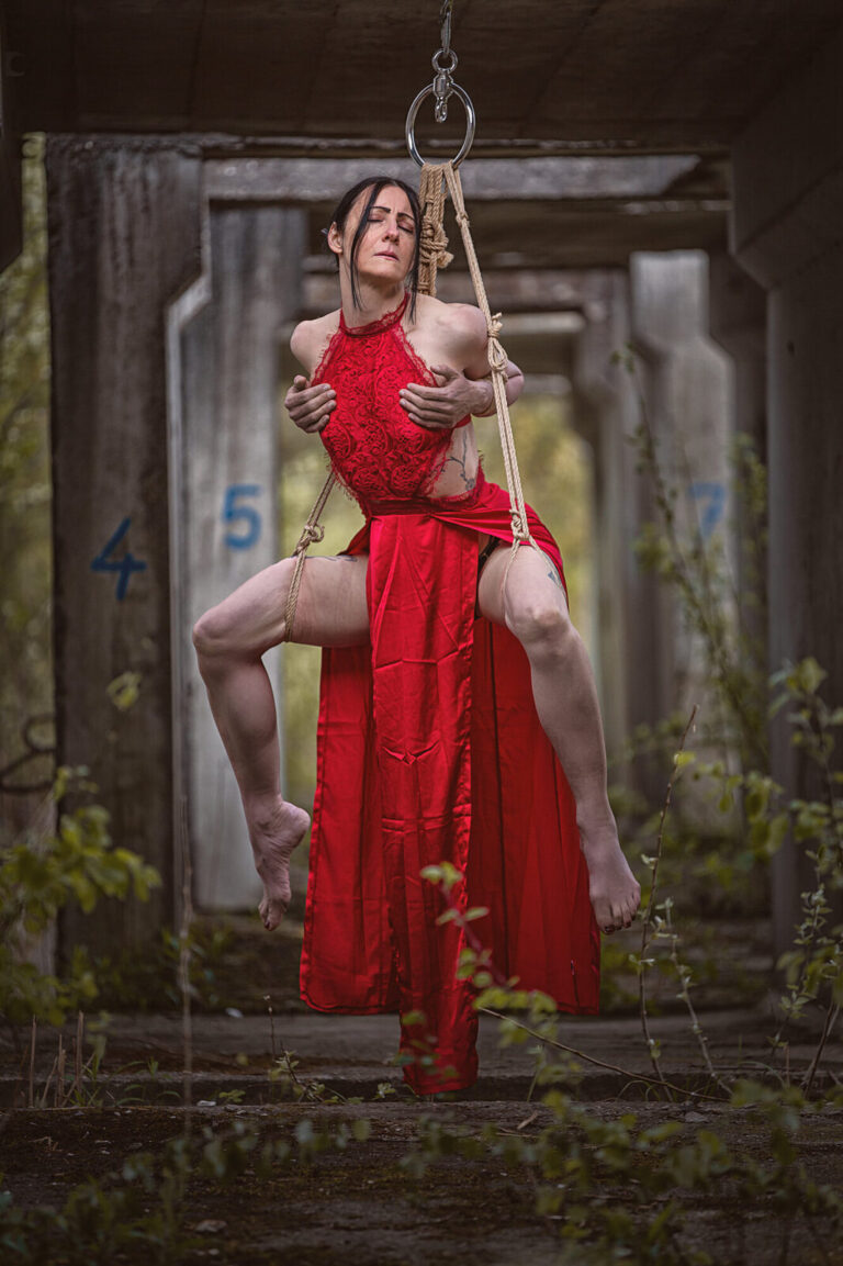 Model im roten Kleid in einer Hängefesselung in einem verlassenen Gebäude
