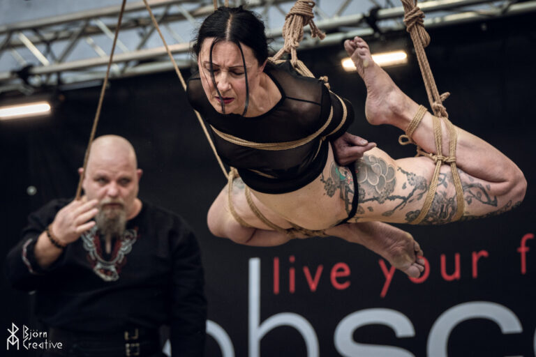 Das Model schwebt waagerecht im Seil, der Rigger hält sie von hinten, obscene 2025
