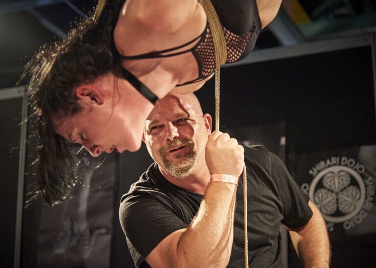 Der Rigger hält das Seil, das Model hängt kopfüber dicht neben ihm, BoundCon 2018